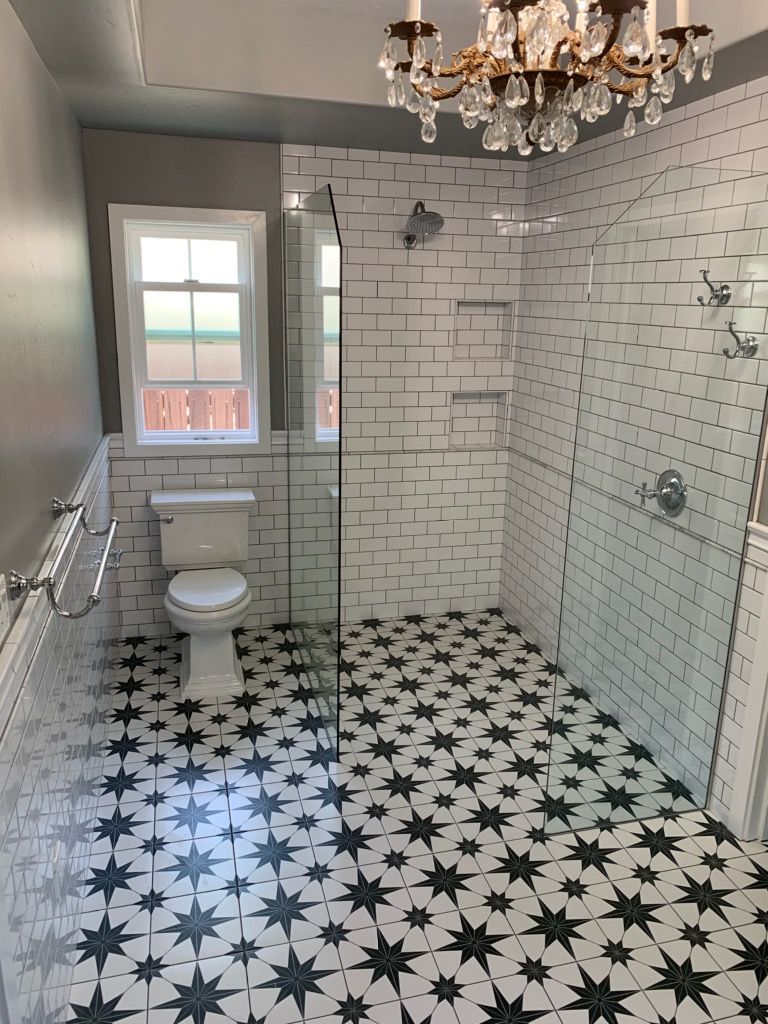 Bathroom with white brick tile shower, patterned floor, toilet, and chandelier.