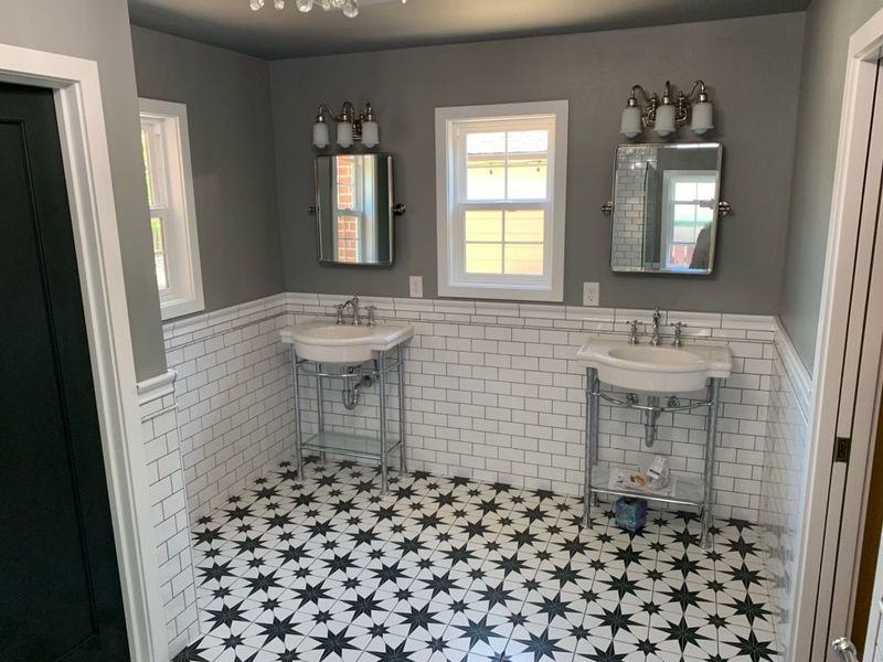 Bathroom with patterned black and white floor, two sinks with mirrors, and white tiled walls.