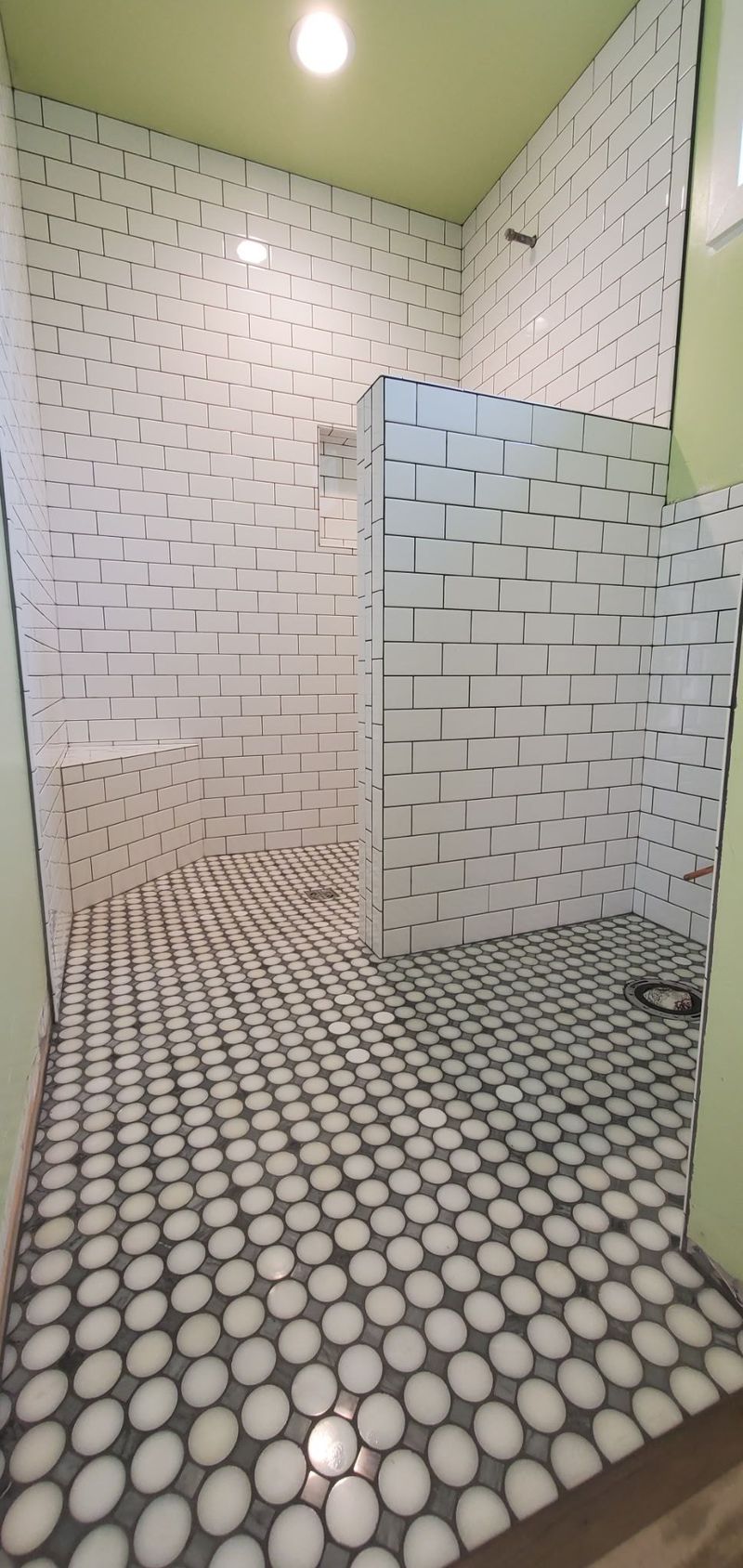 A bathroom with white and black patterned walls and floor, and green walls. A single light is in the ceiling.