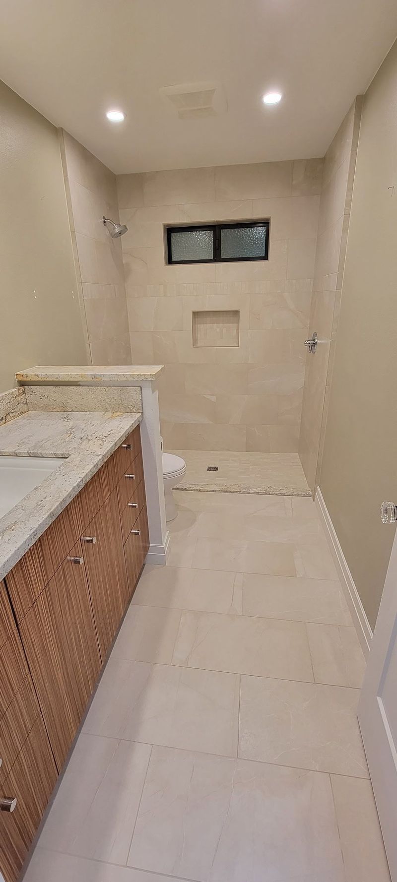 Bathroom with a long narrow shower, neutral-toned walls, and a granite countertop vanity with a woven cabinet.