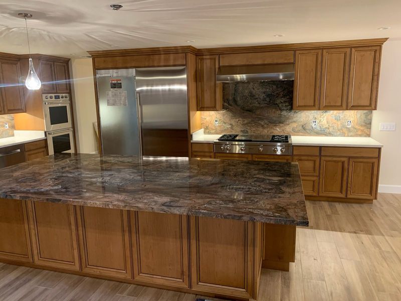 Kitchen with brown cabinets, granite countertops, stainless steel appliances, and wood flooring.