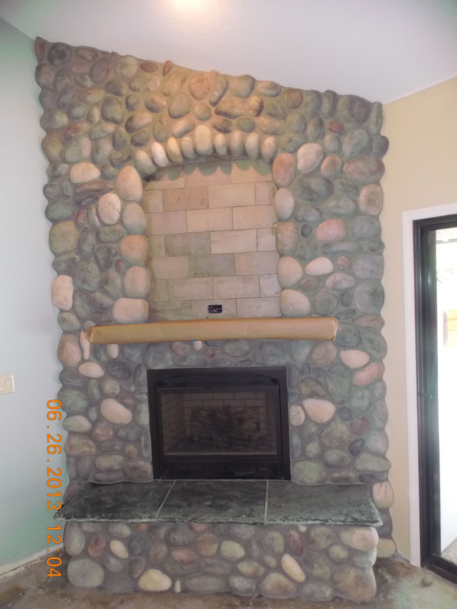 Stone fireplace with a dark framed firebox, topped by a wooden mantle.