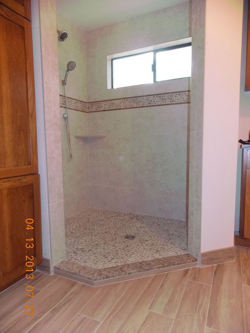 Shower stall with pebble floor, beige tile, glass window, and shower fixtures.