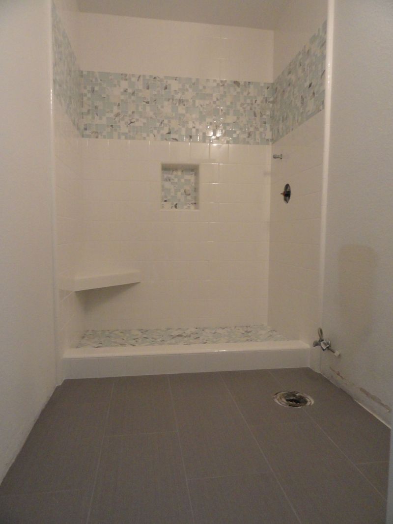 White-tiled shower with a mosaic accent and a built-in seat, a niche, and a grey floor.