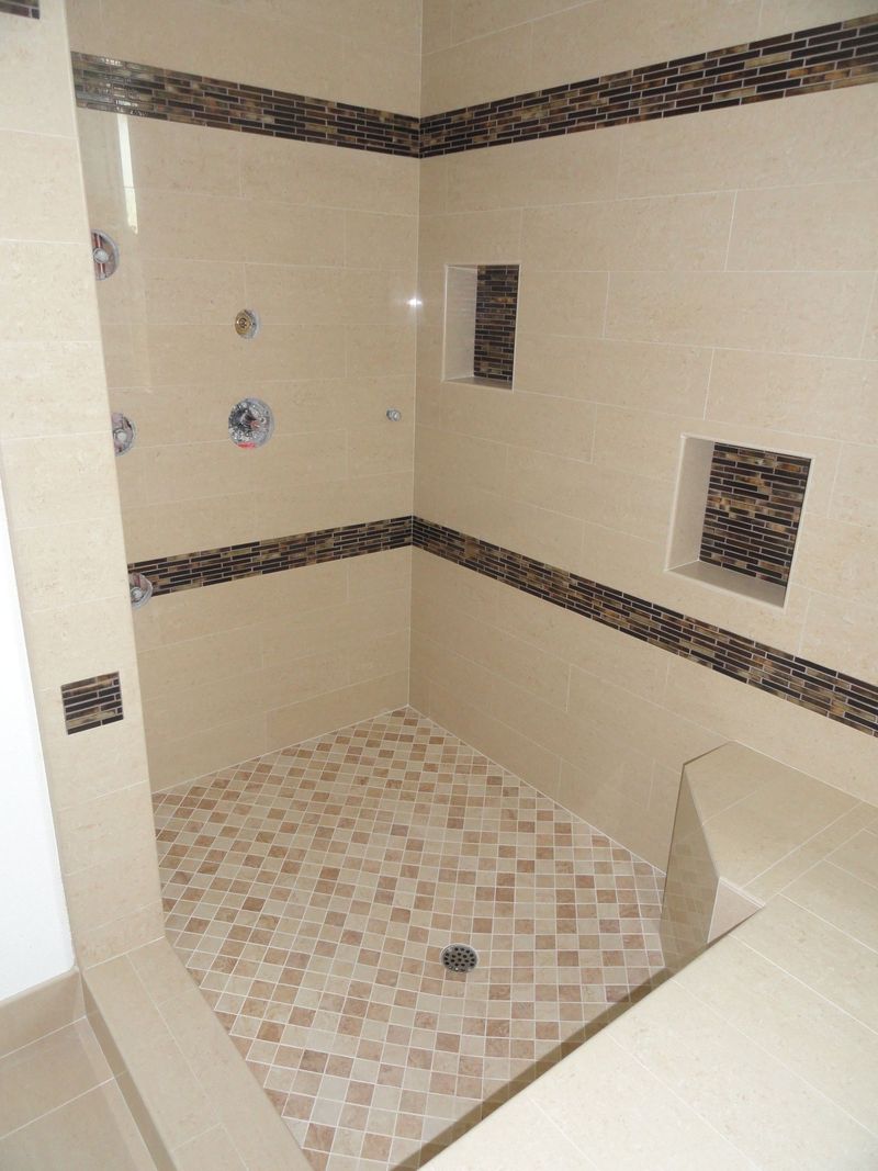 Tiled shower with beige walls, mosaic floor, and dark brown accent trim. Features a built-in bench and recessed shelves.