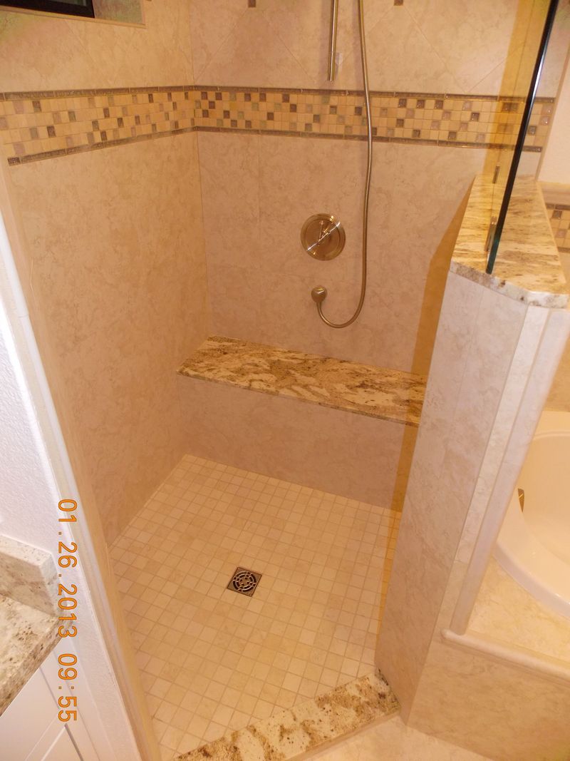 Shower stall with beige tiles, a granite shelf, and decorative mosaic tile band.