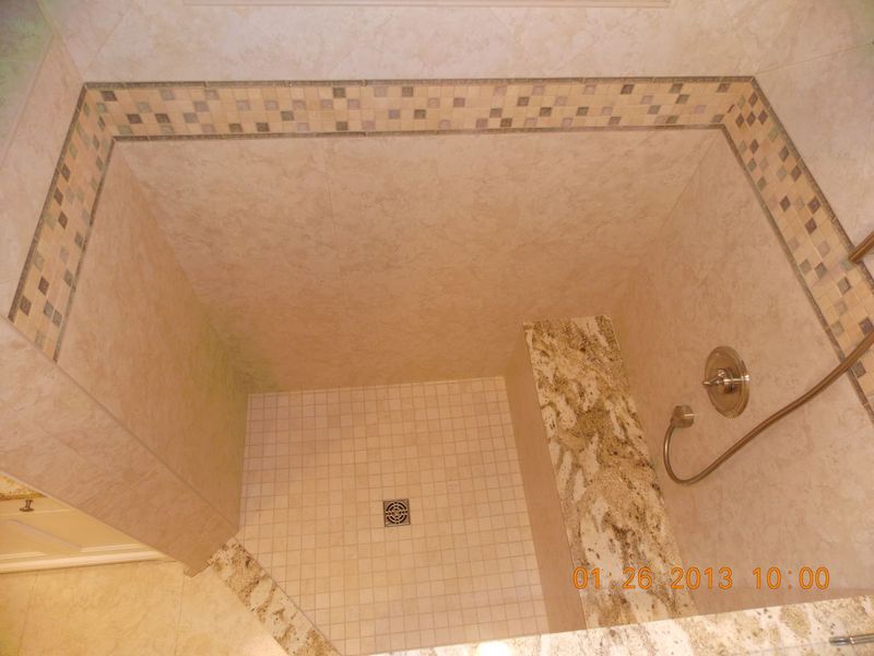 Shower interior with beige and mosaic tile accents; water fixtures on wall.