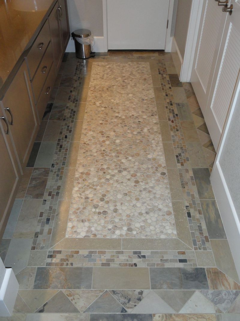 Tiled bathroom floor with pebble-like center, framed by border tiles and stone-look rectangular tiles.