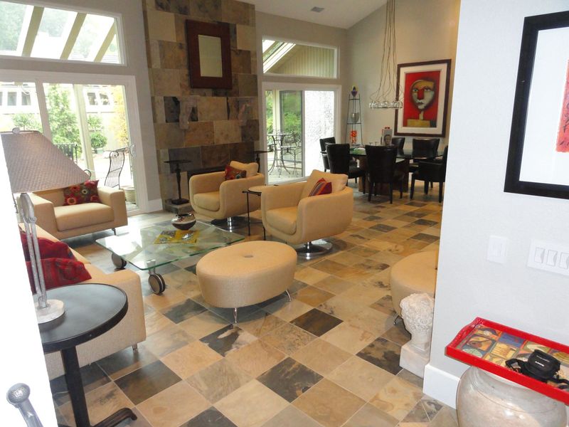 Living room with stone fireplace, beige furniture, and checkered floor. Dining area with dark chairs visible.