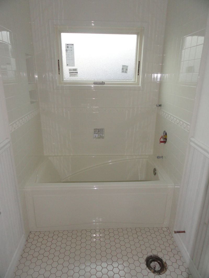 White tiled bathroom with tub and window. Hexagonal floor tiles.