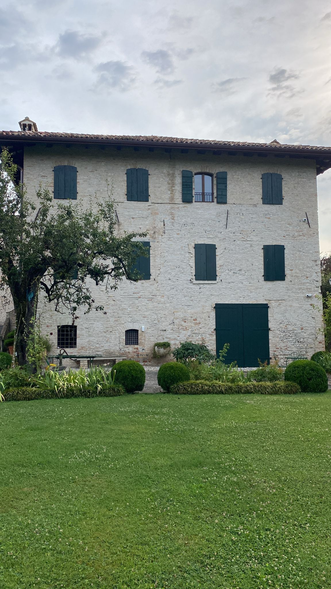 Una grande casa in pietra bianca con una porta verde e un prato verde rigoglioso di fronte.