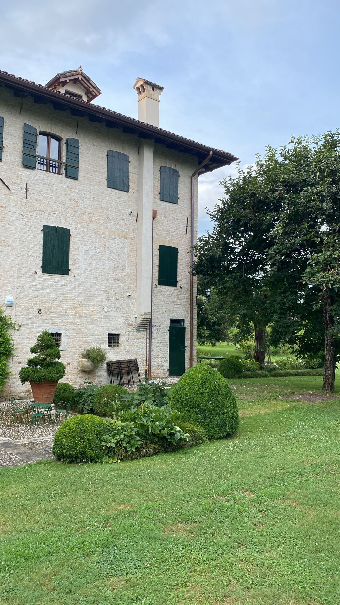Una grande casa in pietra bianca con persiane verdi e un grande prato davanti.