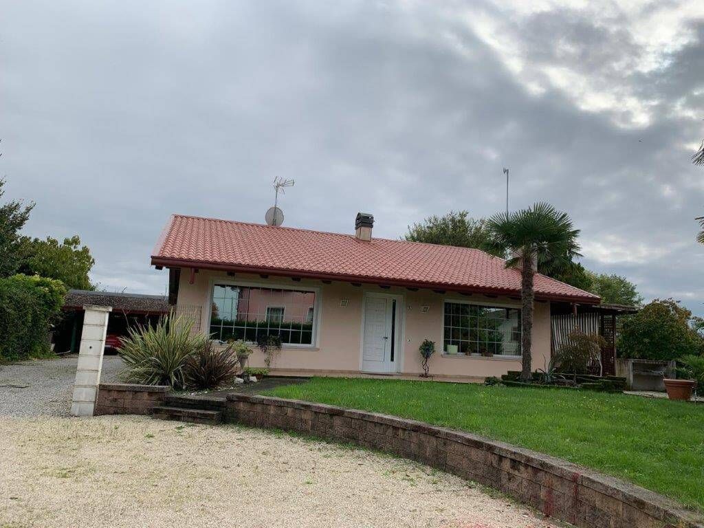 Una casa con il tetto rosso si trova in cima a una collina verdeggiante.