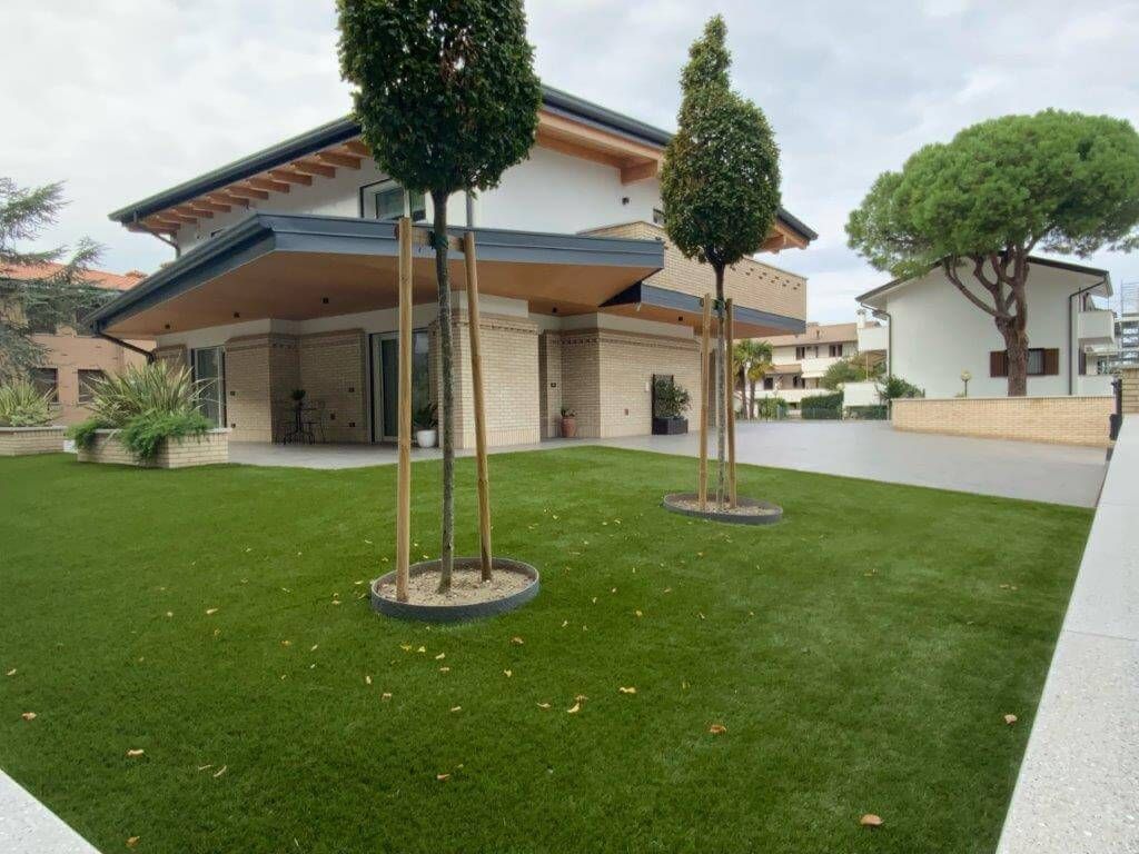Una grande casa con un prato verde lussureggiante e alberi di fronte