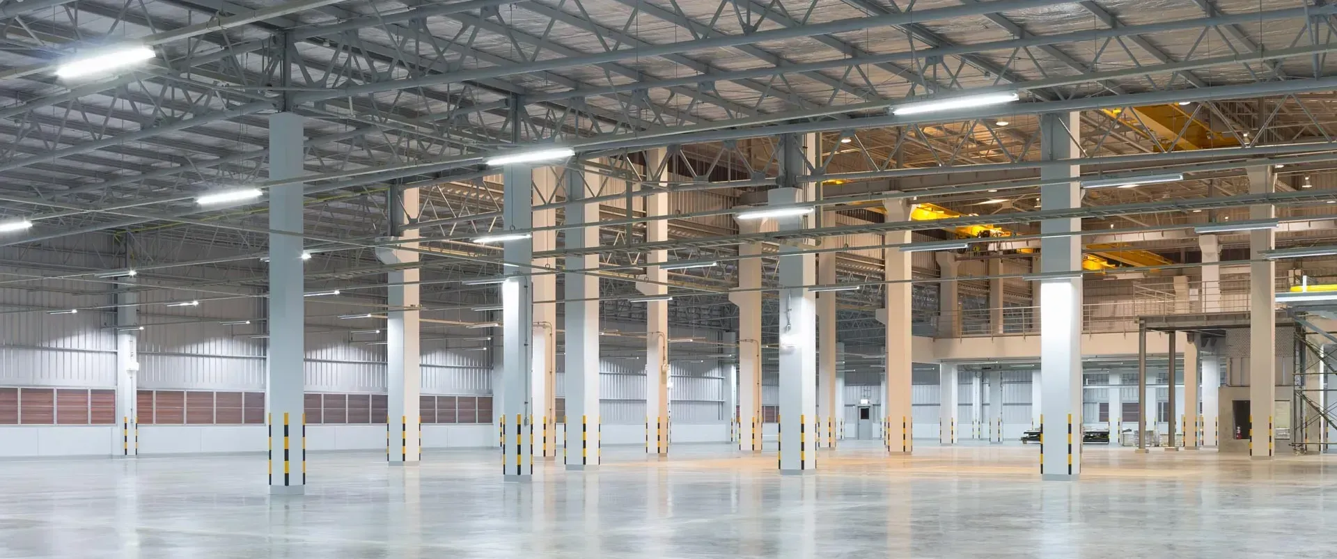 Empty warehouse interior with steel beams, white columns, and polished concrete floor