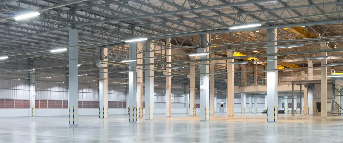 Empty warehouse interior with steel beams, white columns, and polished concrete floor