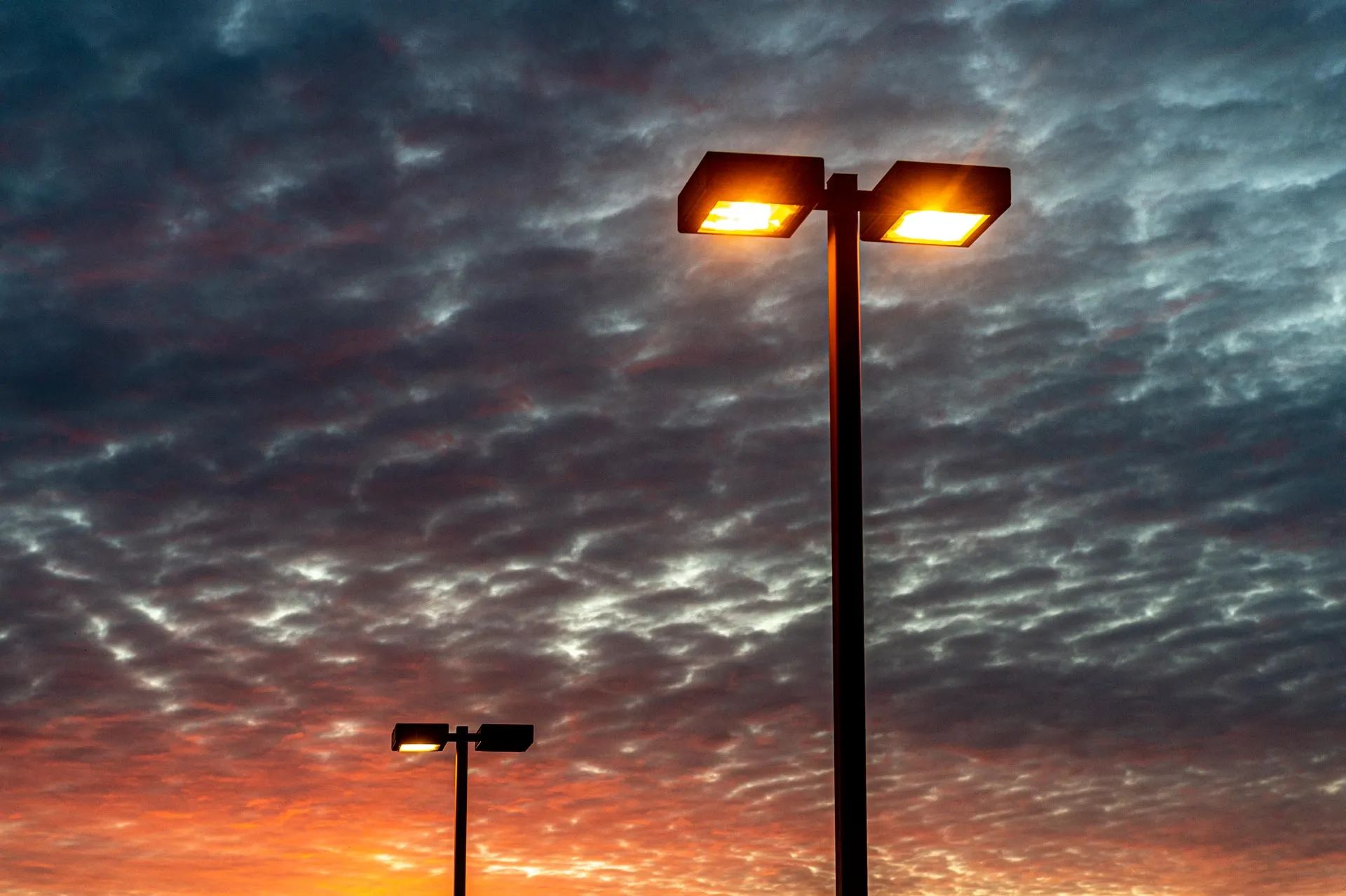 Streetlights glowing at dusk beneath a dramatic cloudy sky with orange light on the horizon