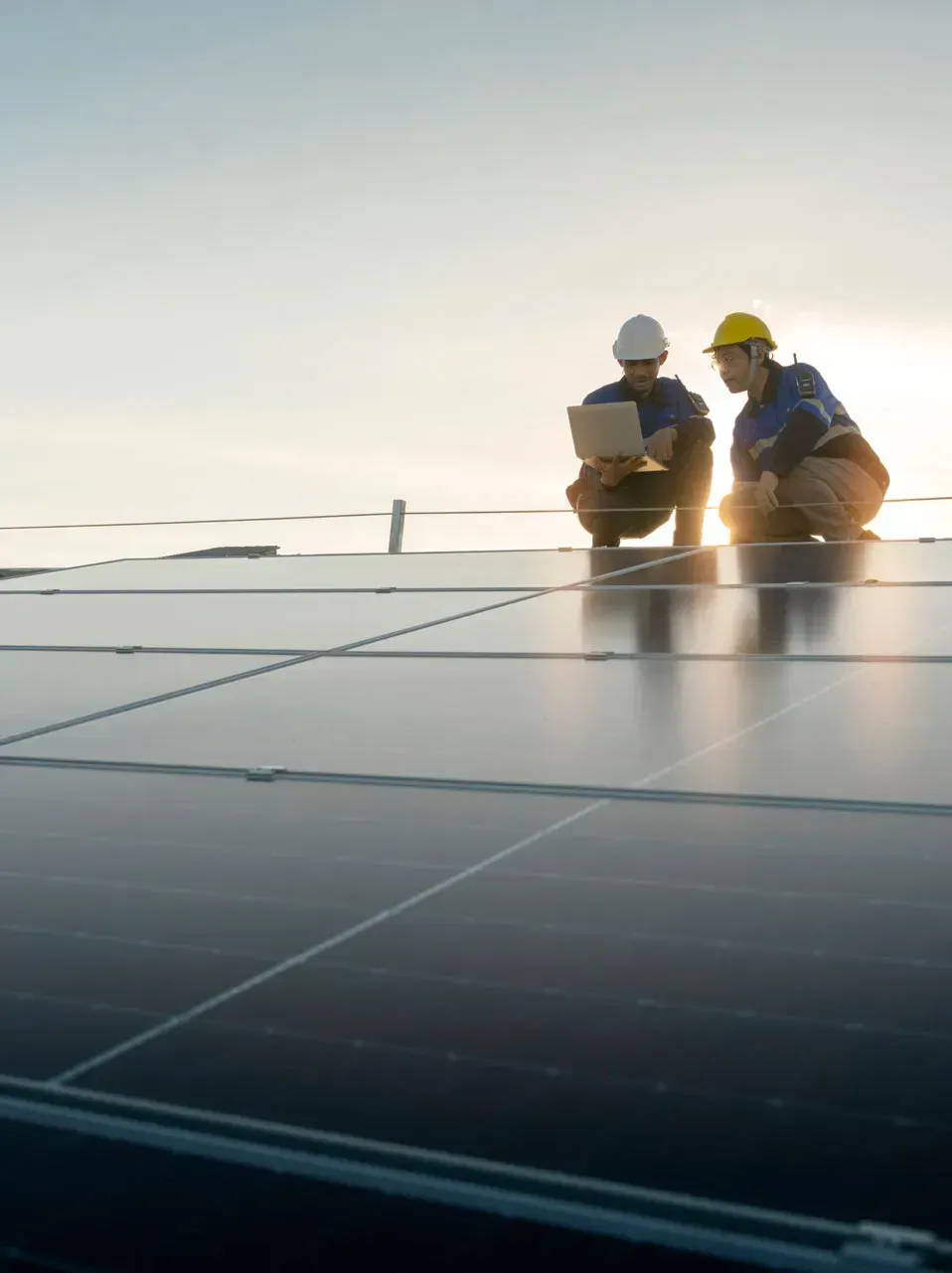 Two workers in hard hats inspecting solar panels at sunset