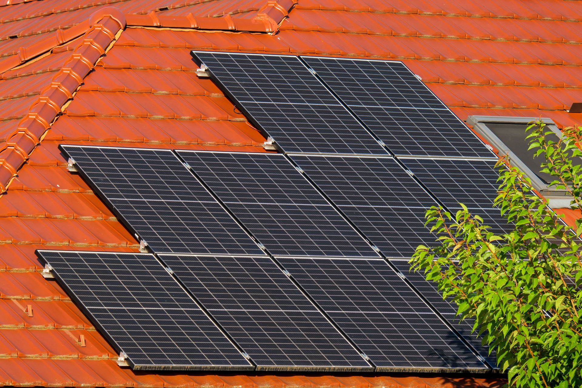 Solar panels mounted on a red tiled roof, with a tree partially visible beside them