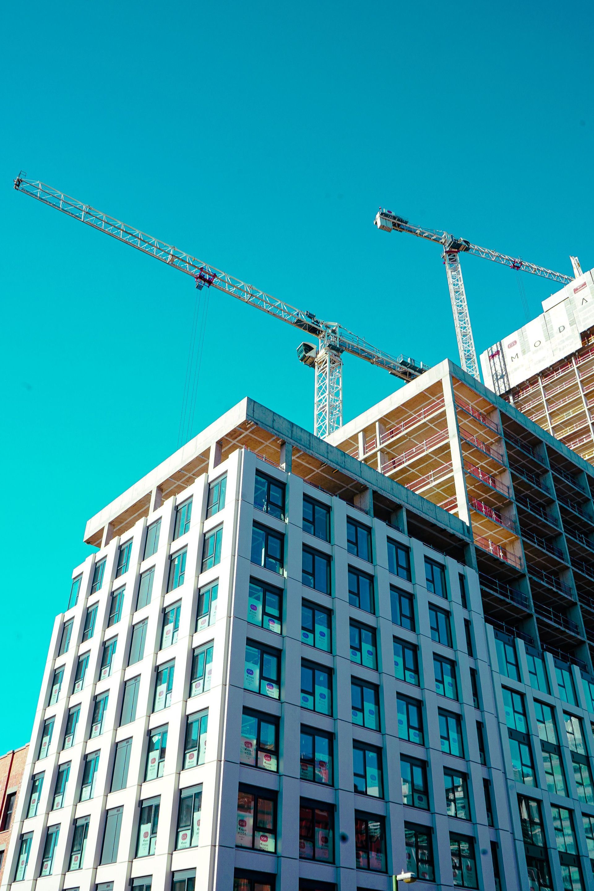High-rise building under construction with two cranes against a clear blue sky