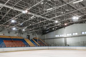 Indoor ice rink with empty stands, bright overhead lights, and a blue and orange seating section