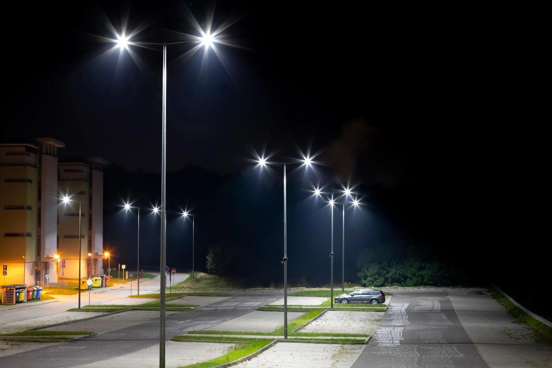 Empty parking lot and apartment buildings at night, lit by tall streetlights.