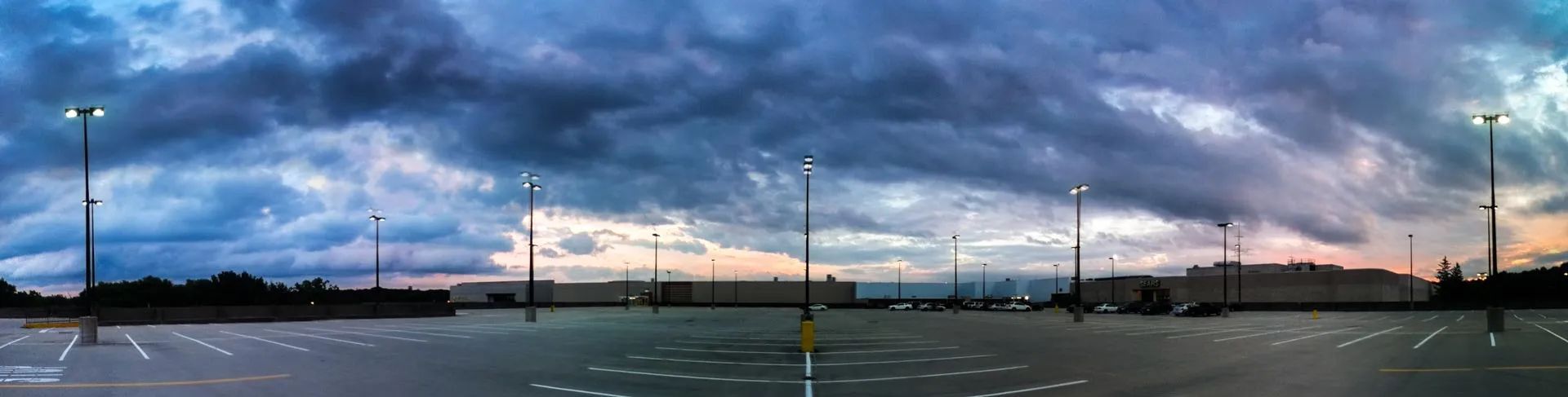 Wide sunset sky over a parking lot with streetlights and silhouetted distant buildings.