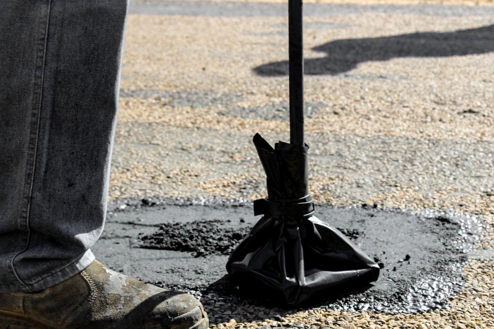 A jackhammer breaks asphalt beside a worker’s boot on a street repair site.