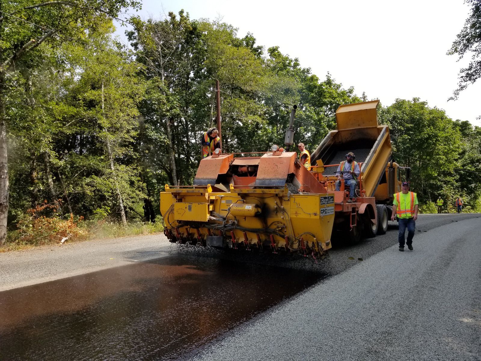 Road crew paving a rural road with a yellow asphalt paver and workers nearby