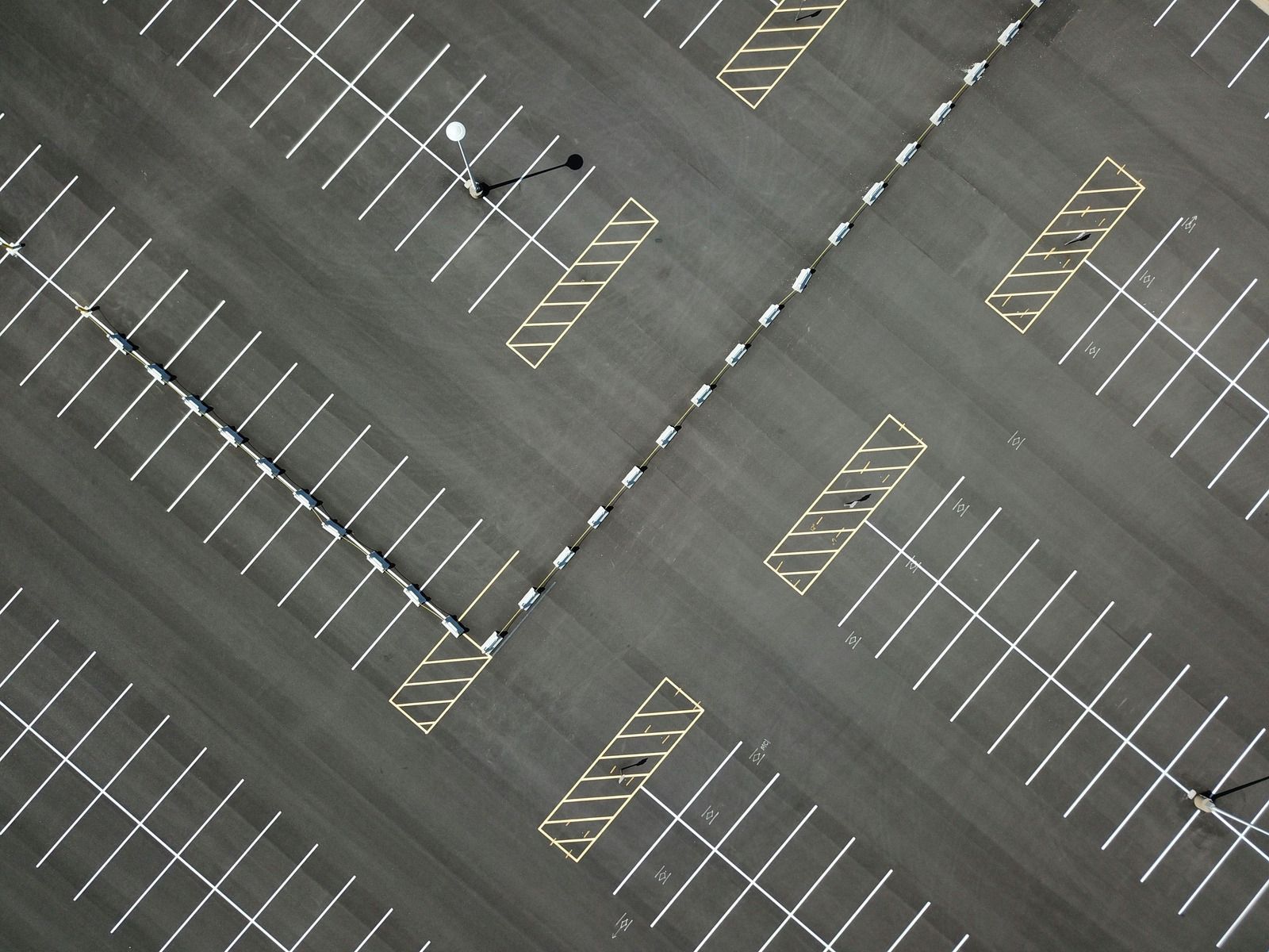 Diagonal aerial view of an empty parking lot with white and yellow painted spaces and two small vehicles