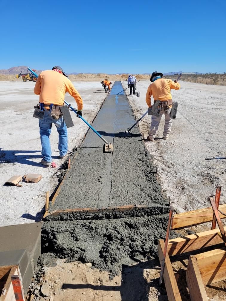 Construction workers smoothing fresh concrete on a long roadway under a clear blue sky.