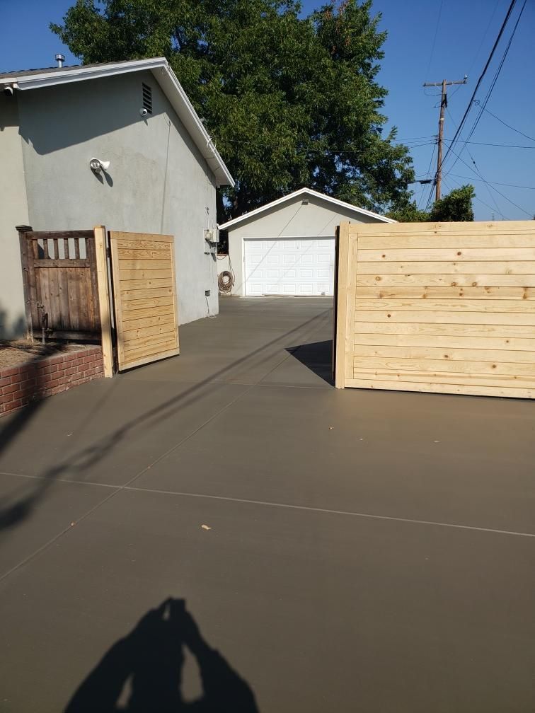 Driveway beside a house with wooden fencing and gates, leading to a white garage under a clear blue sky.