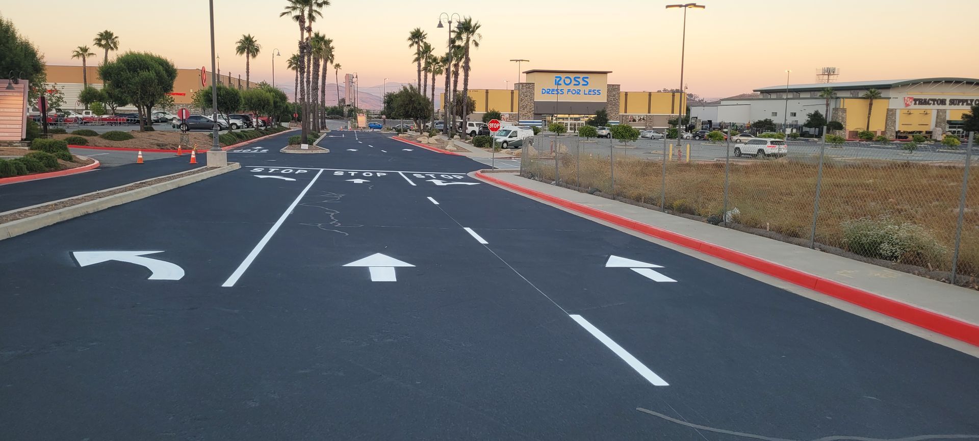 Empty multi-lane road at sunset with white lane arrows and a red curb on the right