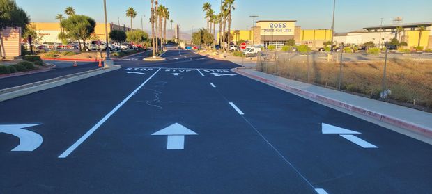 Road with white directional arrows and lane markings, bordered by dry grass and buildings at sunset.