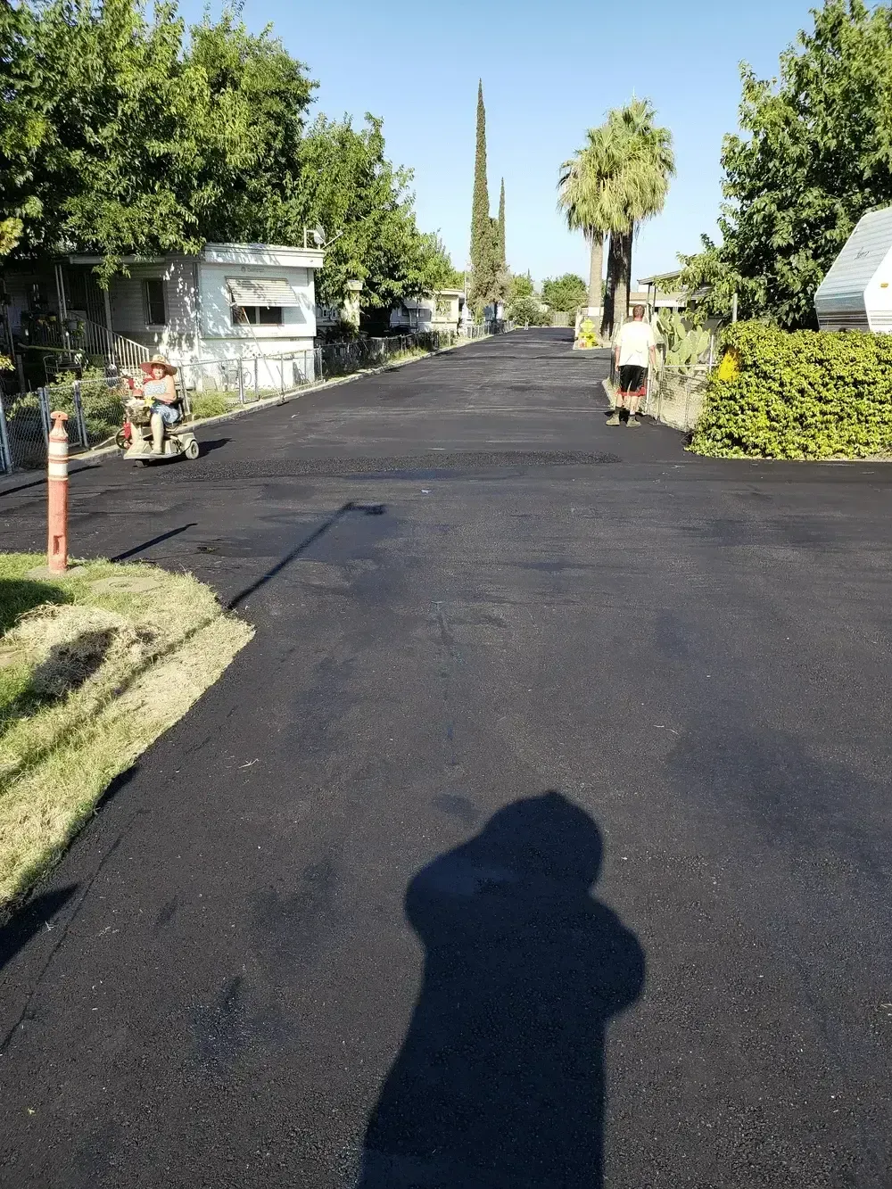 Residential street with fresh black asphalt, utility poles, houses, and a sidewalk under a clear blue sky