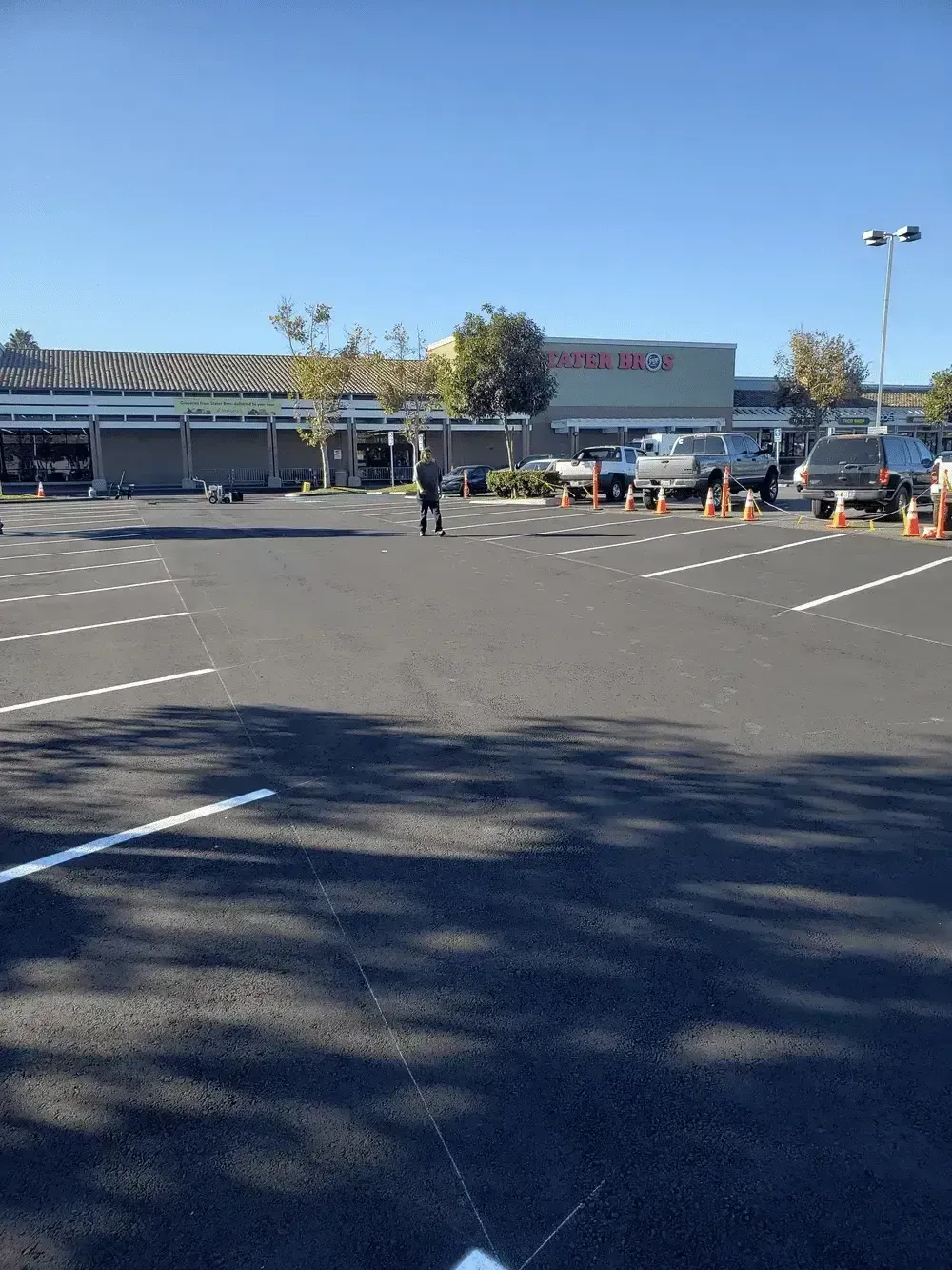 Parking lot in front of a store with a few people and traffic cones on a sunny day
