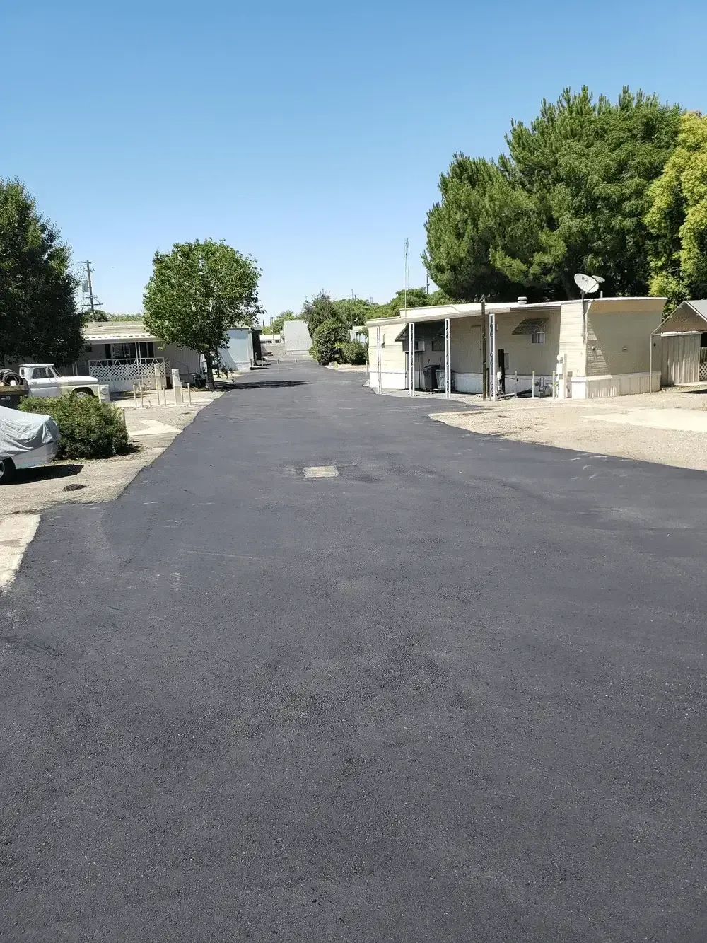 Quiet residential street with a freshly paved black road, trees, and single-story homes on both sides