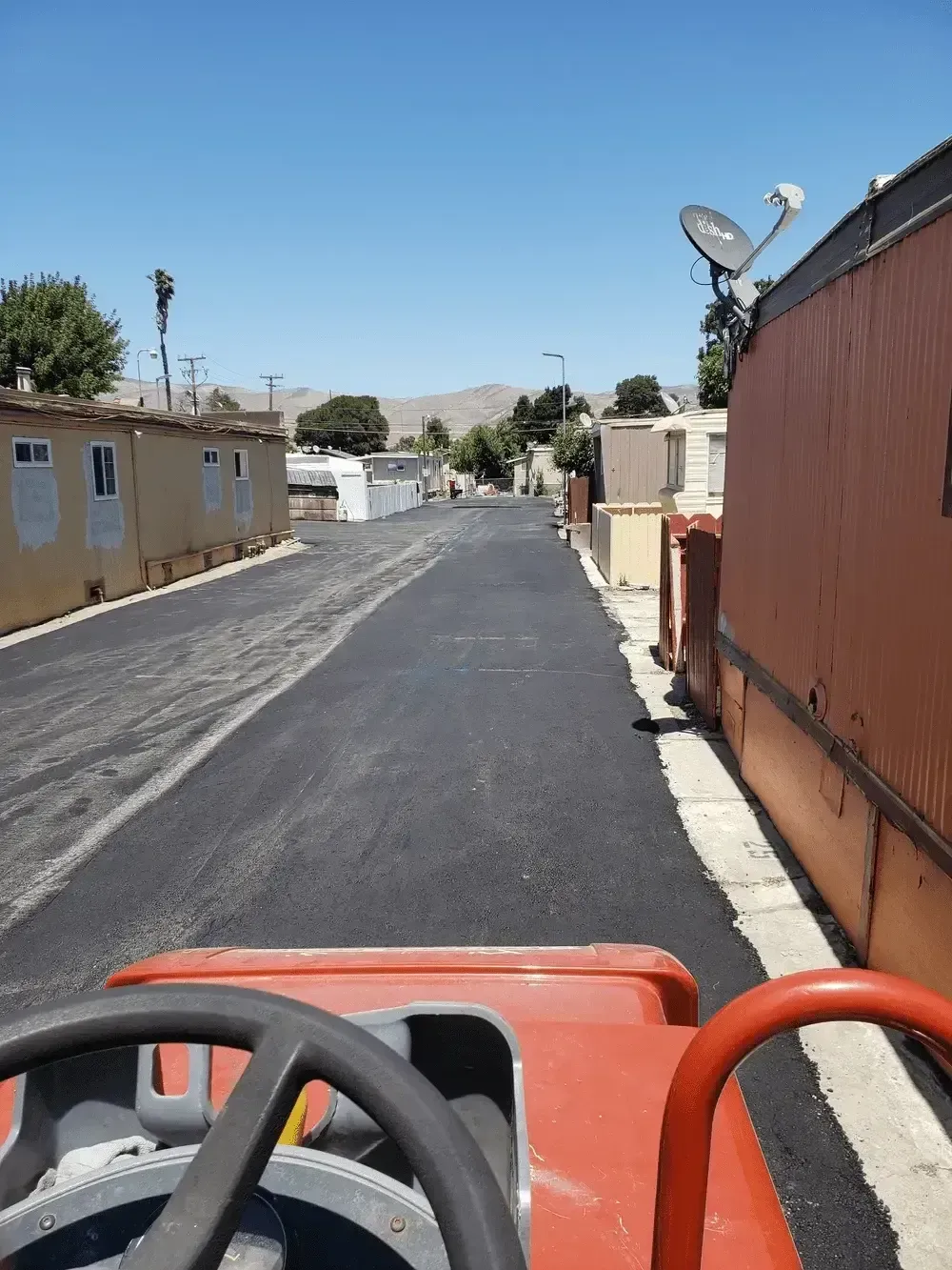 View from a red vehicle on a paved road between tan buildings under a bright sky