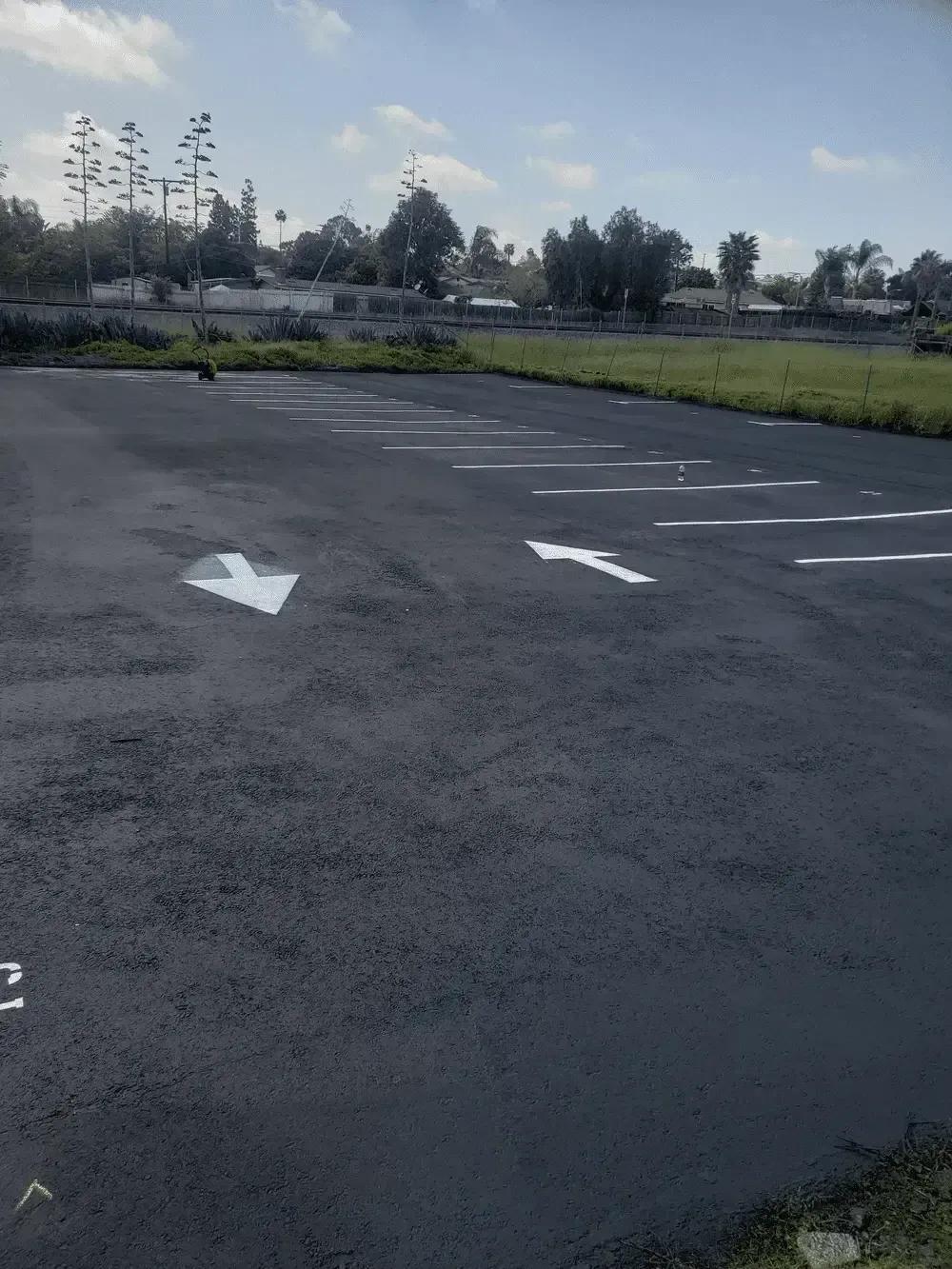 Empty asphalt parking lot with white directional arrows and grassy field beyond