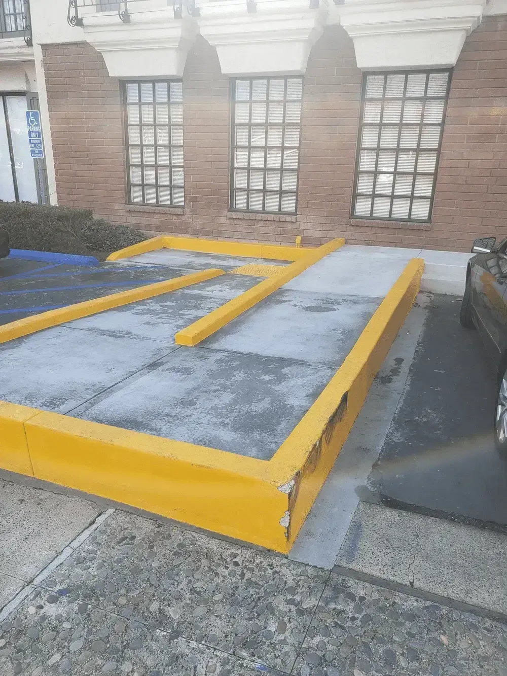 Yellow-painted accessibility platform/ramp beside a brick building with windows and stone steps