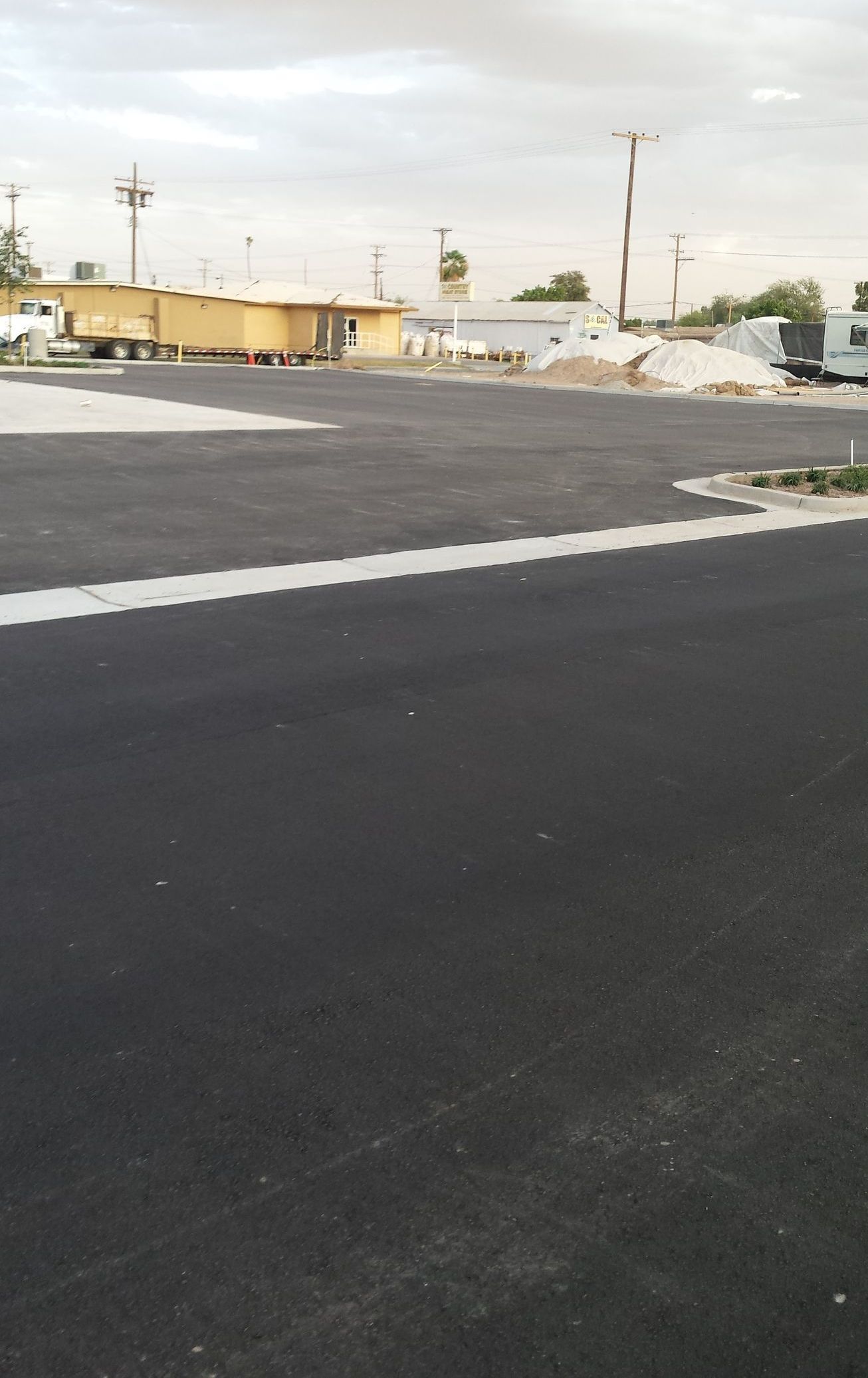 Empty parking lot beside a low yellow building and piles of white material under a cloudy sky