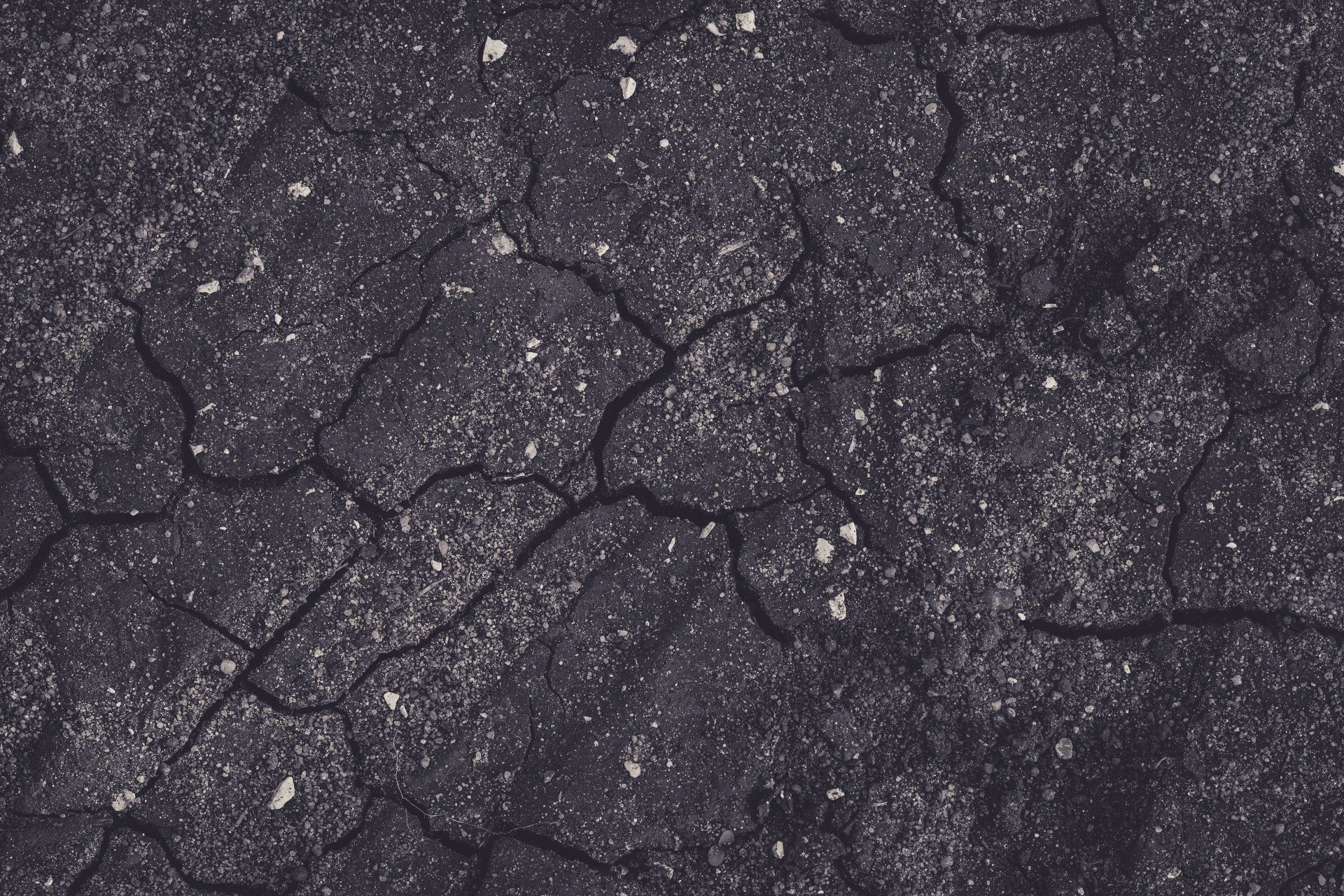 Dark cracked asphalt with scattered small white specks