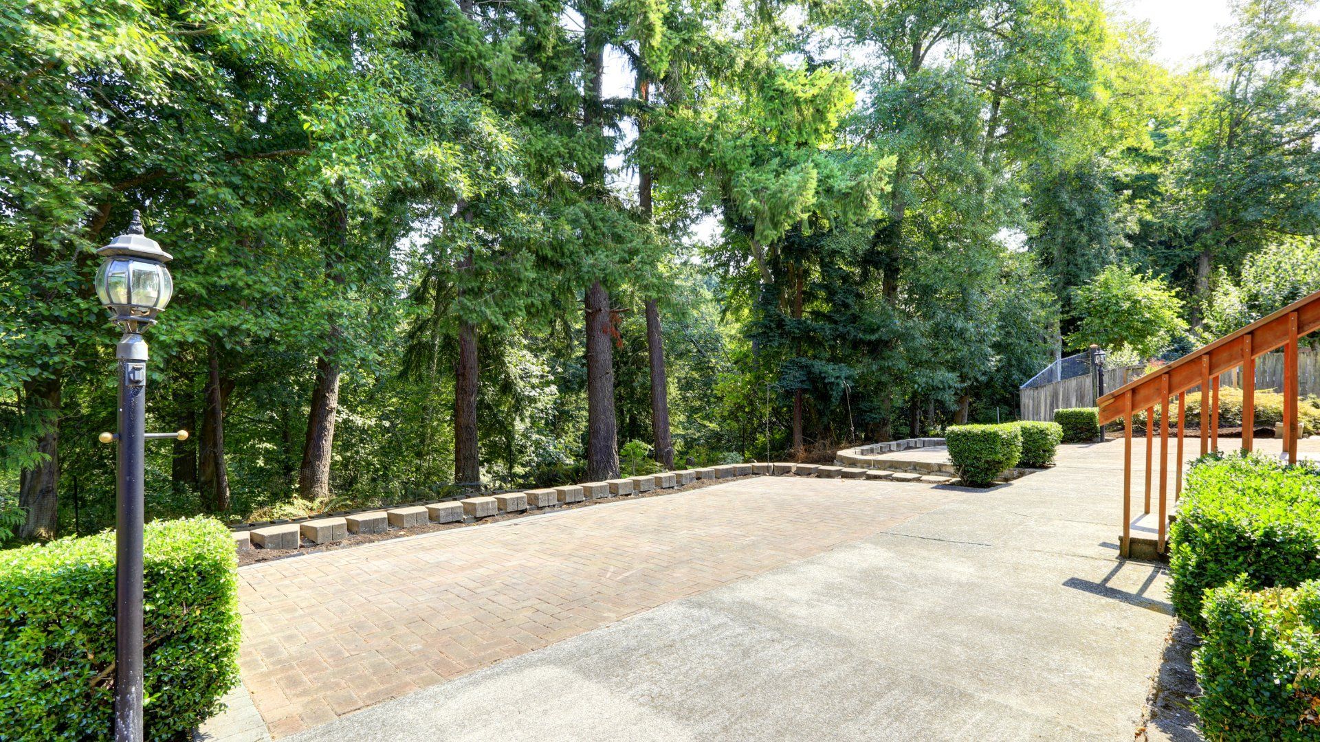 Stairs leading from a deck to a large concrete patio. The patio has nice landscaping around it with bushes.