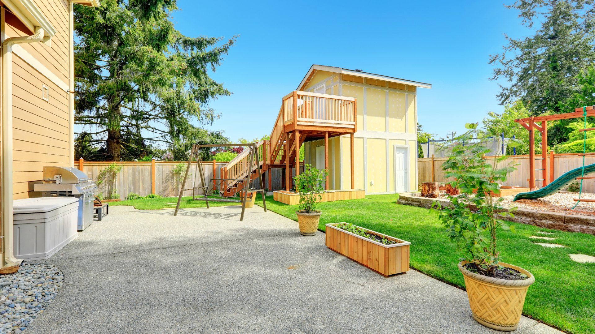 Backyard with a guest house, playground structure and planters. There is a concrete patio attached to the house.