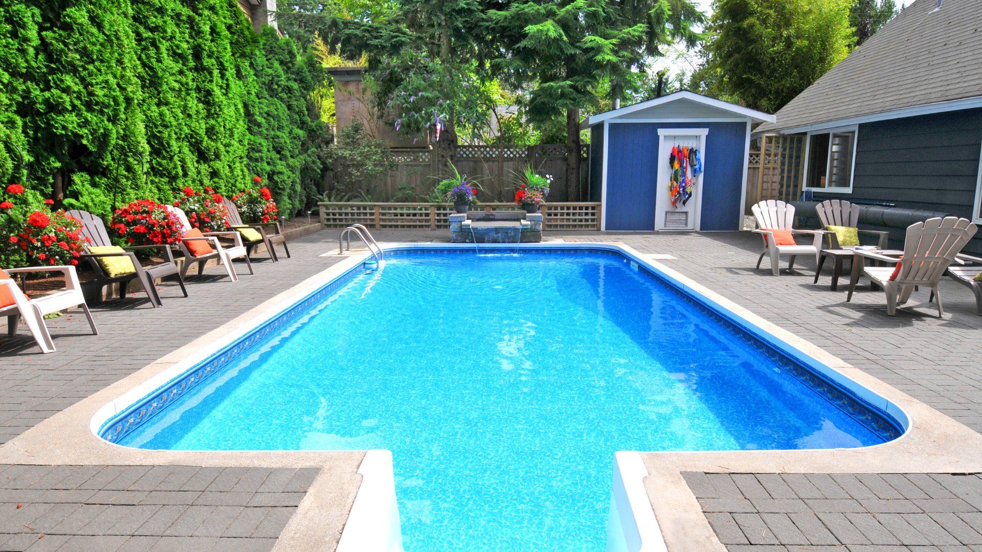 Overlooking a backyard pool surrounded by a concrete pool deck. The backyard has a variety of patio furniture and a pool shed.