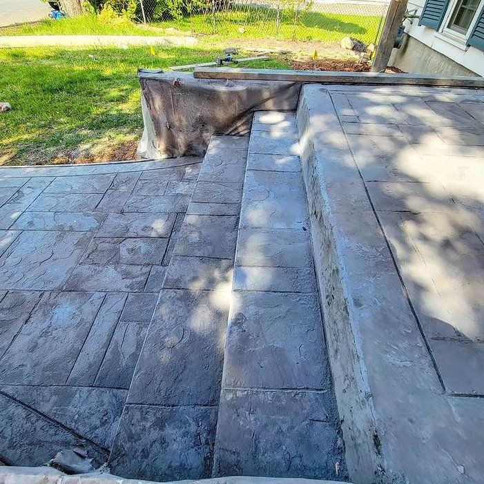 Concrete steps leading up to a concrete landing. The steps lead to a stamped concrete walkway.