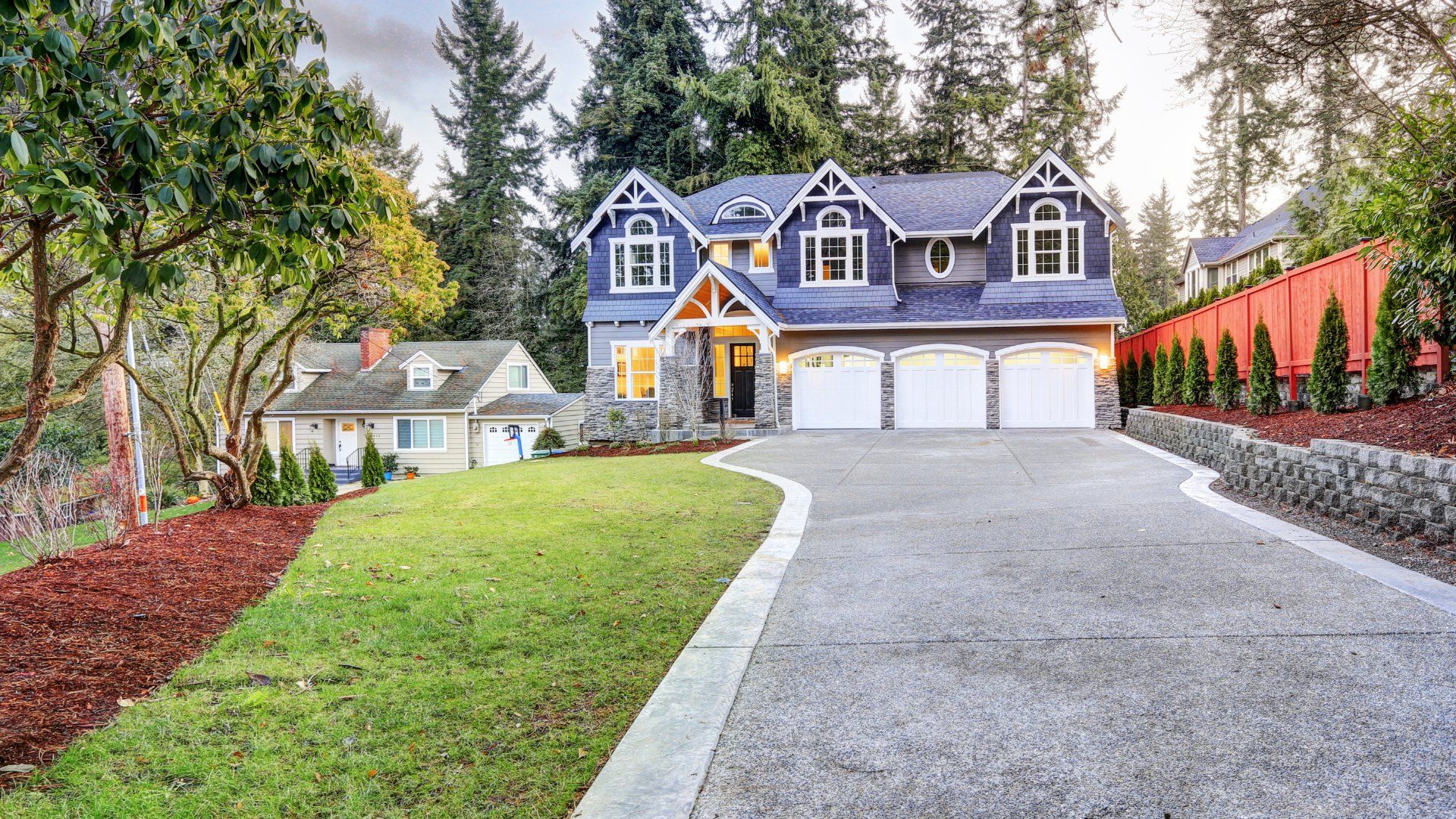 Long concrete driveway leading up to a modern looking blue and grey house.  The driveway is lined with a concrete border and nice landscaping.