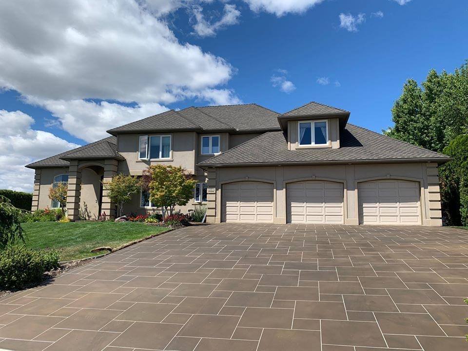 Stamped concrete driveway with neat design.  The driveway is in front of a large house with a three car garage.