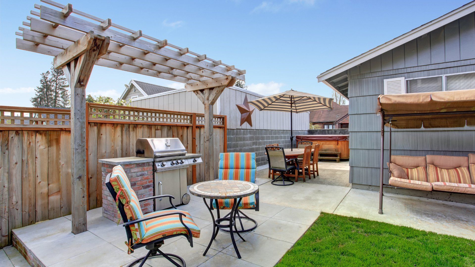 Stamped concrete backyard patio.  The patio is in a small backyard with an outdoor kitchen, swinging chair and other patio furniture.