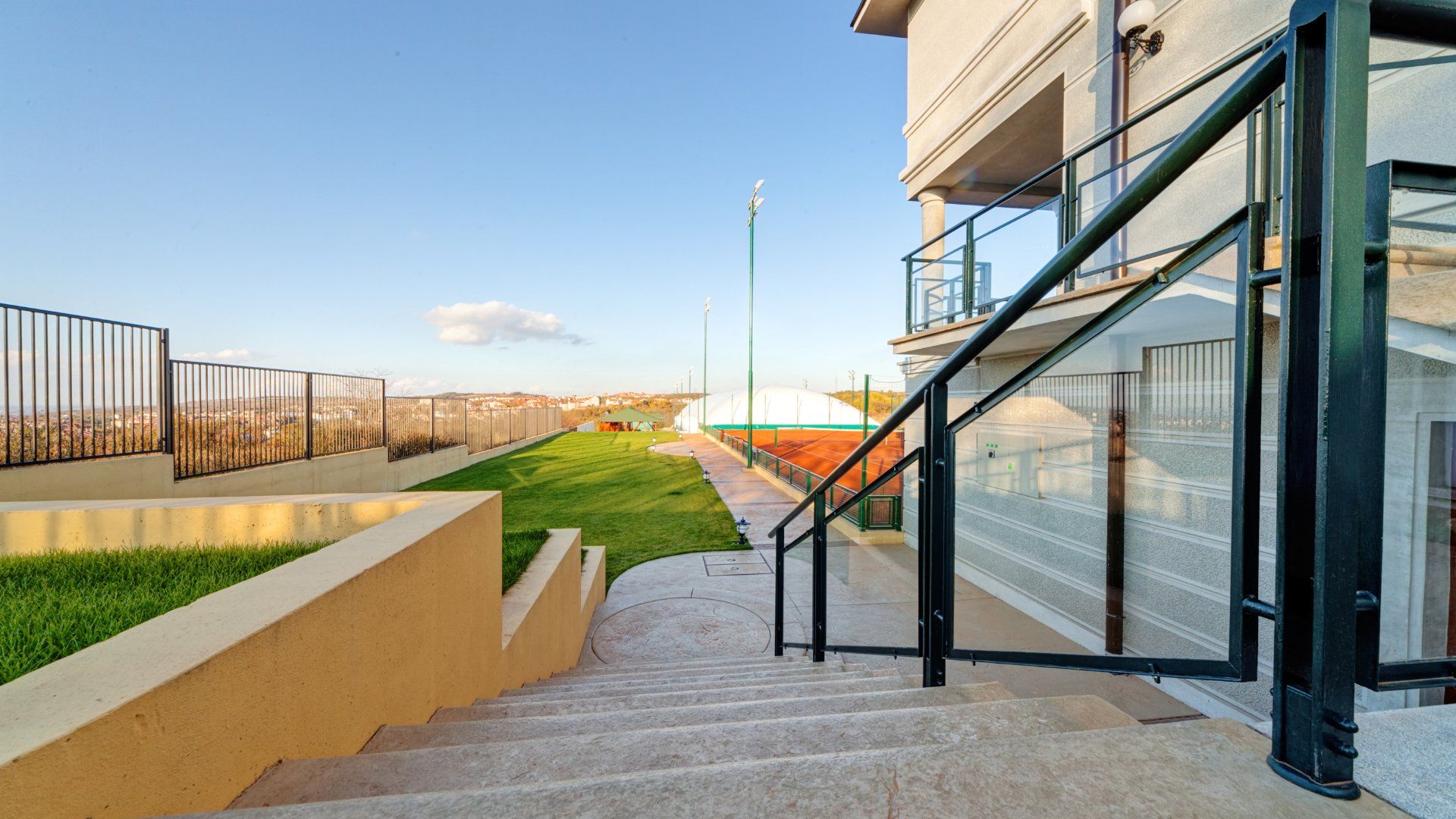 Concrete steps with a black handrail leading down to a green space.  The stairs appear to be next to a condo or commercial building.